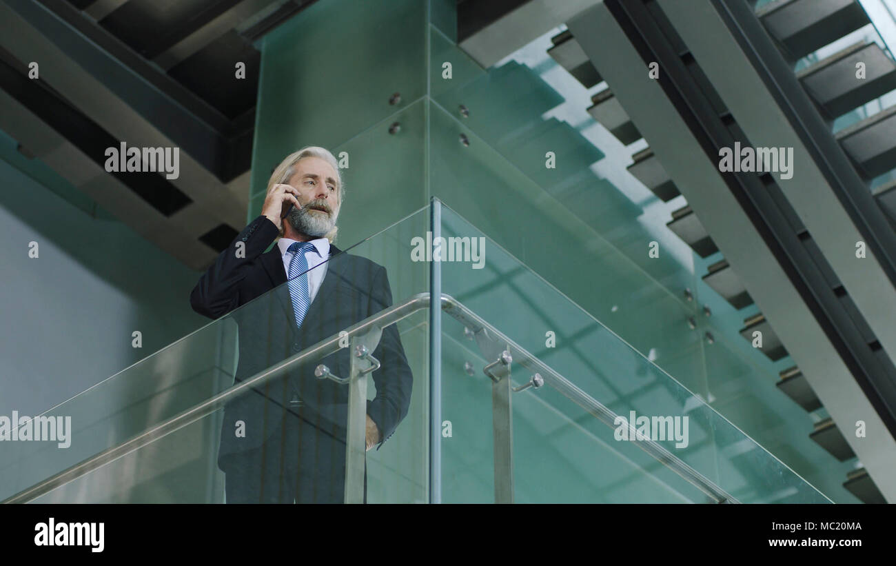 Senior Corporate Executive stehen im zweiten Stock in modernen Büro Anrufen über Handy Gebäude. Stockfoto