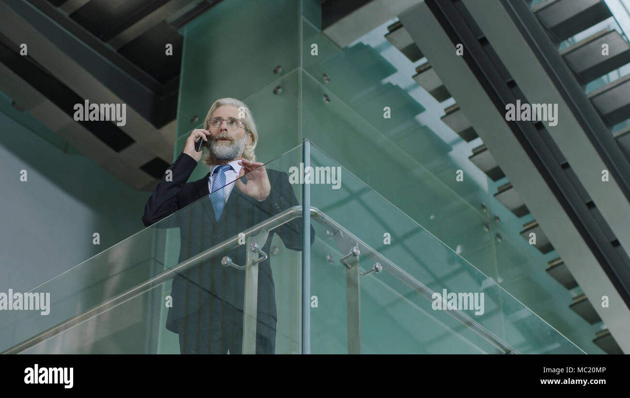 Senior Corporate Executive stehen im zweiten Stock in modernen Büro Anrufen über Handy Gebäude. Stockfoto
