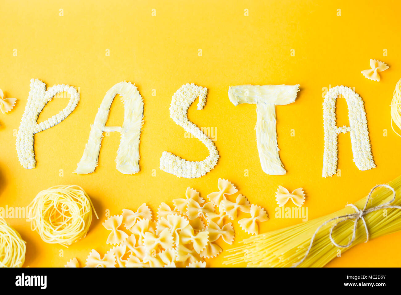 Das Wort "Pasta wird in Massen Briefe von kleinen rohen Makkaroni auf gelbem Hintergrund festgelegt sind neben einer Vielzahl von Arten von Pasta. Essen auf einem hellen backgr Stockfoto