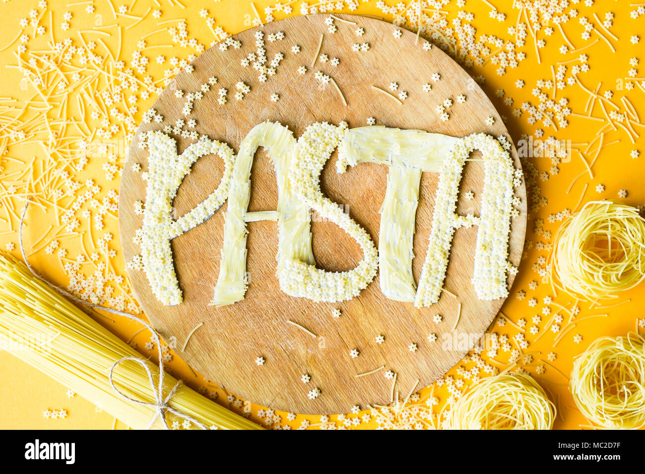 Das Wort "Pasta wird in umfangreichen Briefe von kleinen rohen Makkaroni auf einer hölzernen runde Board unter verschiedenen Arten von Nudeln. Essen auf einem hellen backgr Stockfoto