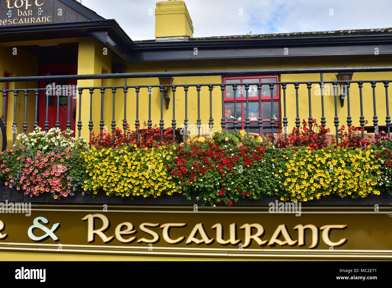 Detail der Veranda mit Metallgeländer und Töpfe Blumen leuchtend gelben Restaurant in der Nähe von Bunratty Castle. Stockfoto