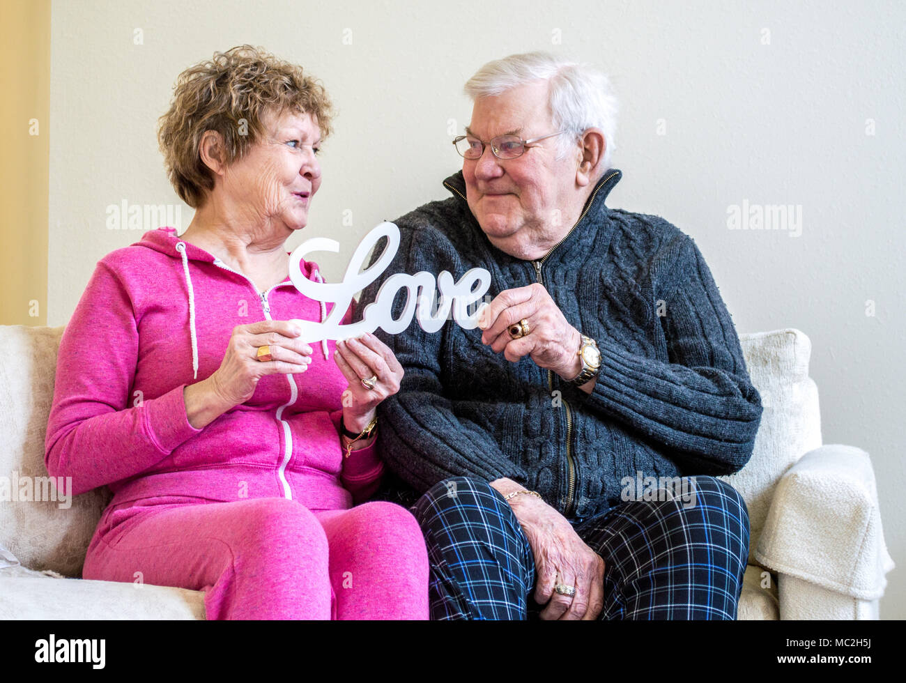 Reifen kaukasischen Paar lächelnd an und halten ein hölzernes Schild mit der Aufschrift 'Liebe' beim Sitzen auf einem Sofa Stockfoto