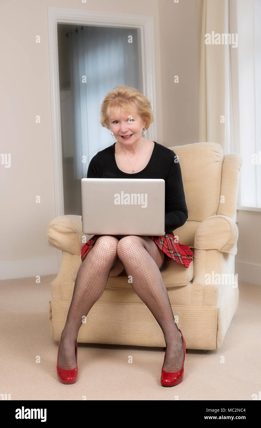 Reife Frau in einem bequemen Sessel sitzend mit einem Laptop. Stockfoto