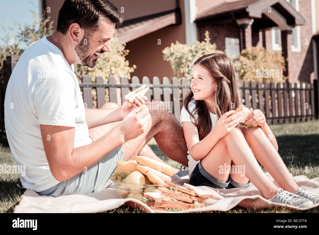 Aufmerksamer Vater Essen ein Sandwich an seine Tochter auf der Suche zufrieden. Stockfoto