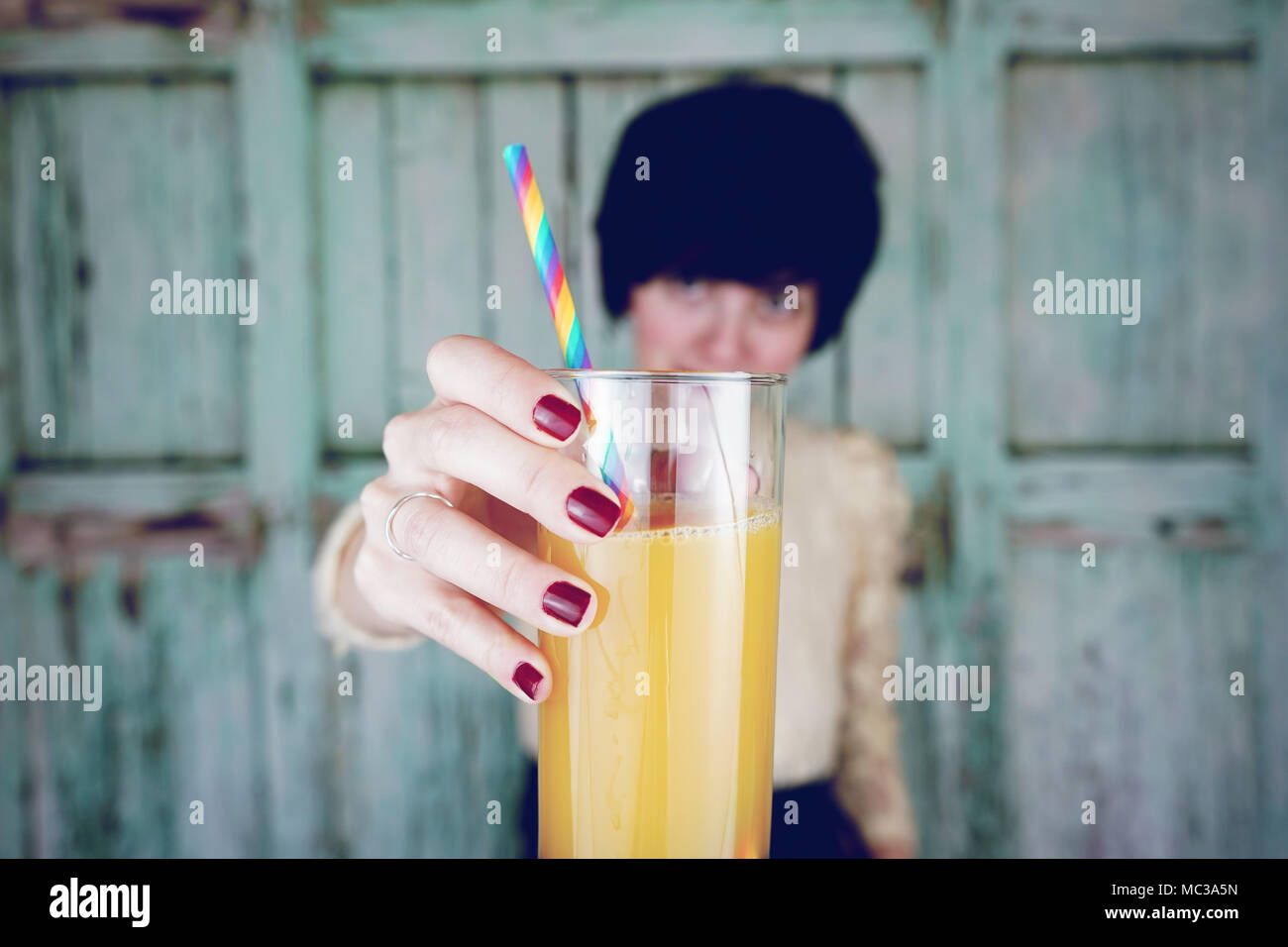 Junge Frau trinkt Orangensaft mit einem Regenbogen Stroh Stockfoto