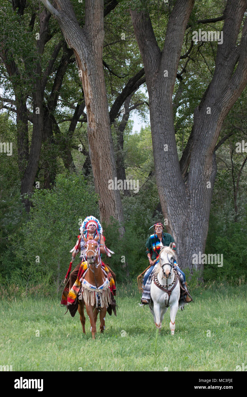 Krieger in Comanche Kleidung Reiten Pferde durch Bäume im Wald Stockfoto