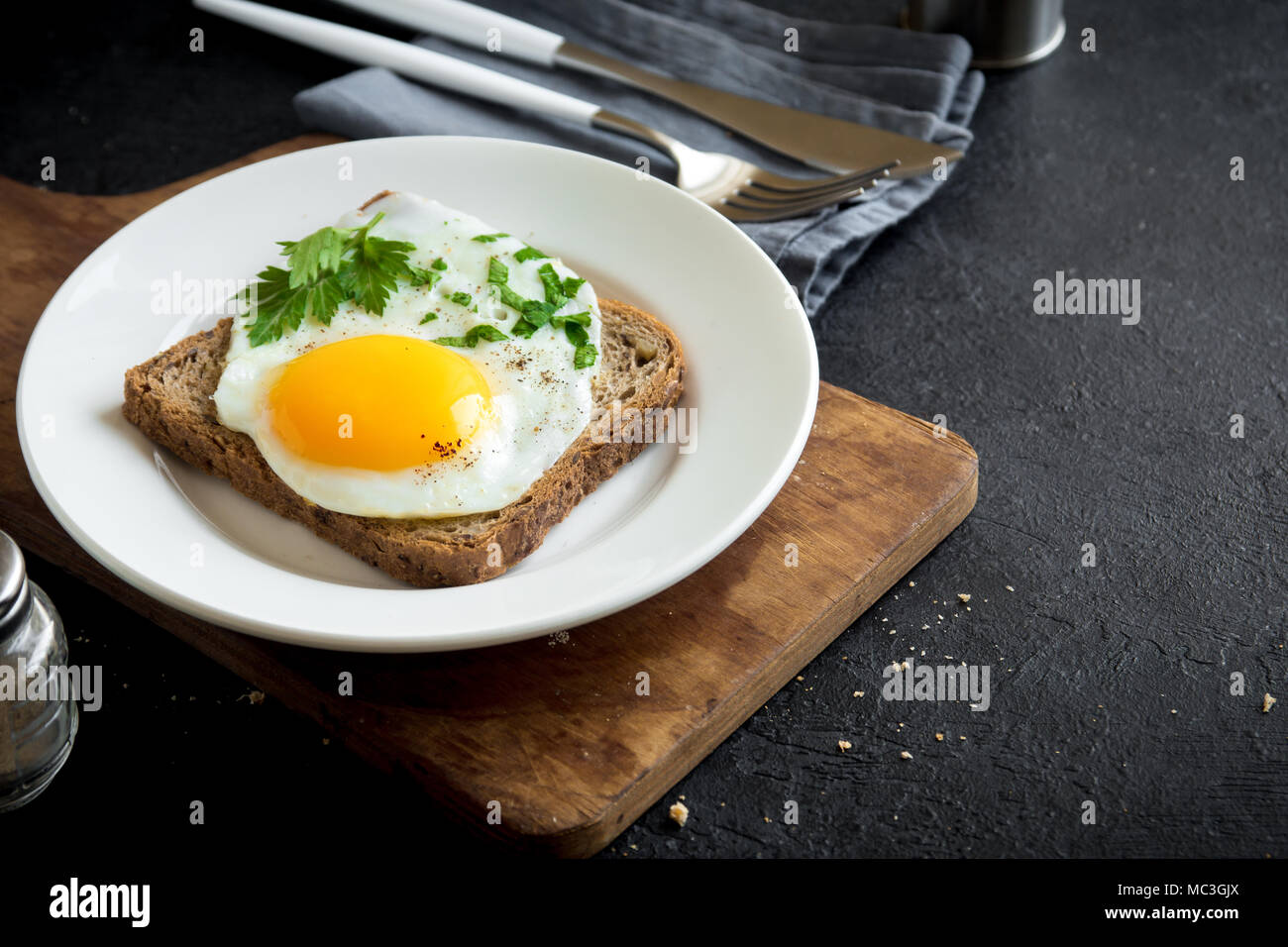 Spiegelei auf Toast zum Frühstück. Spiegelei mit Brot und Petersilie auf weiße Platte auf Schwarz, Ansicht von oben, kopieren. Stockfoto