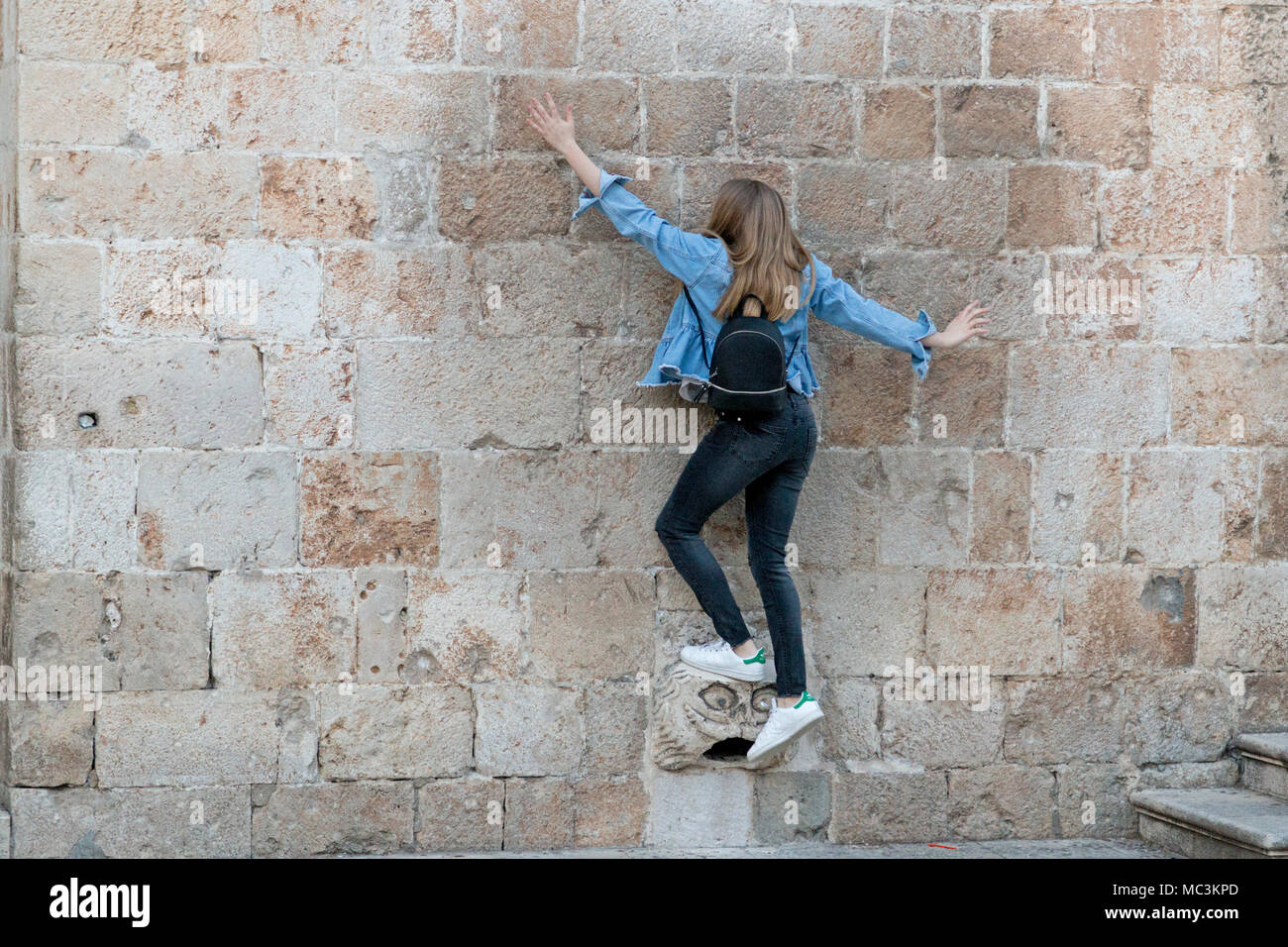 Junge Frau Balancieren auf einem gargoyle Kopf von der Wand, Stradun, Altstadt, Dubrovnik hervorstehende, Kroatien Stockfoto