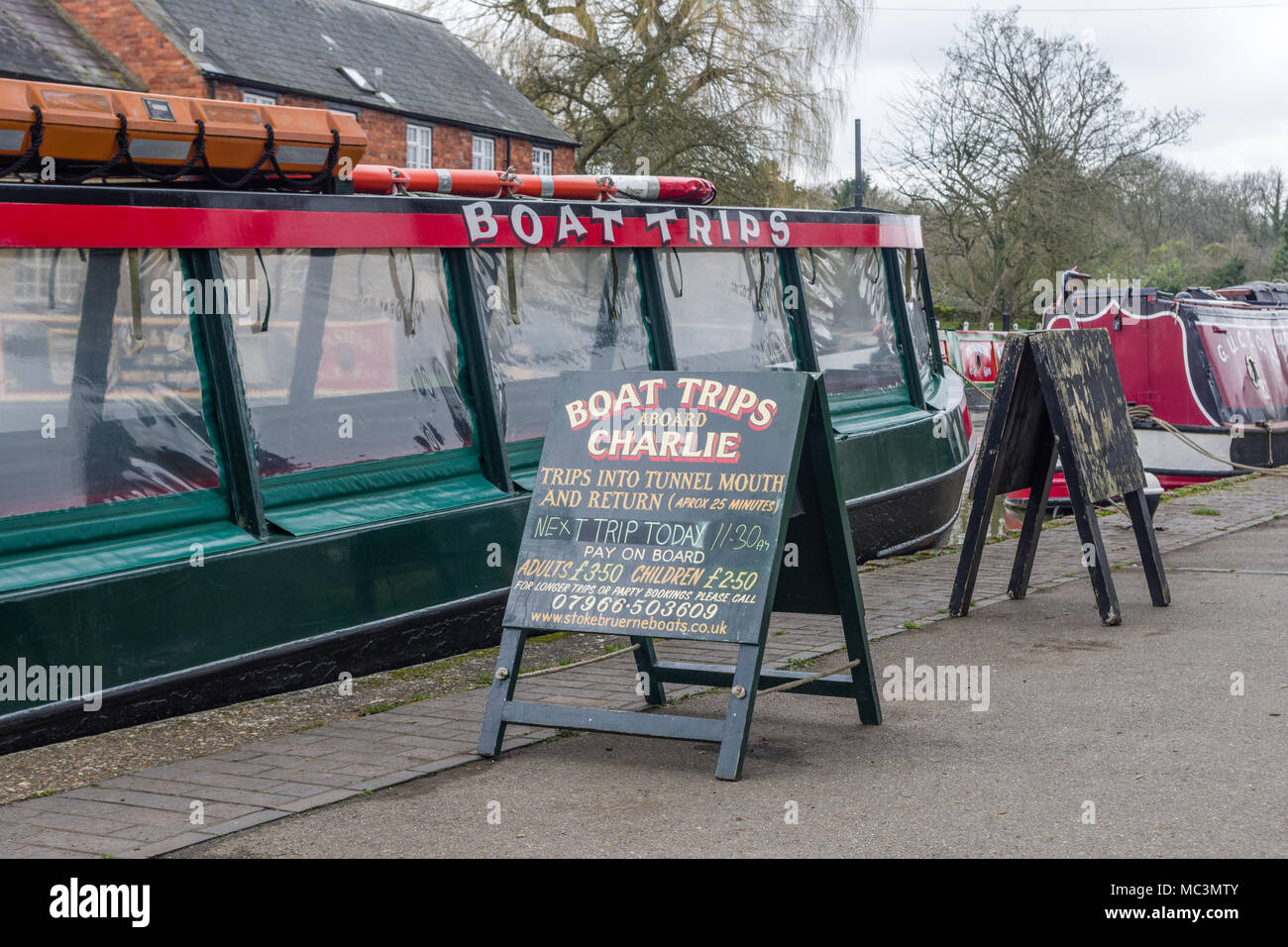 Ein schmales Boot mit dem Namen 'Charlie' mit einem Schild an der Seite Werbung Bootsfahrten; Stoke Bruerne, Northamptonshire, Großbritannien Stockfoto