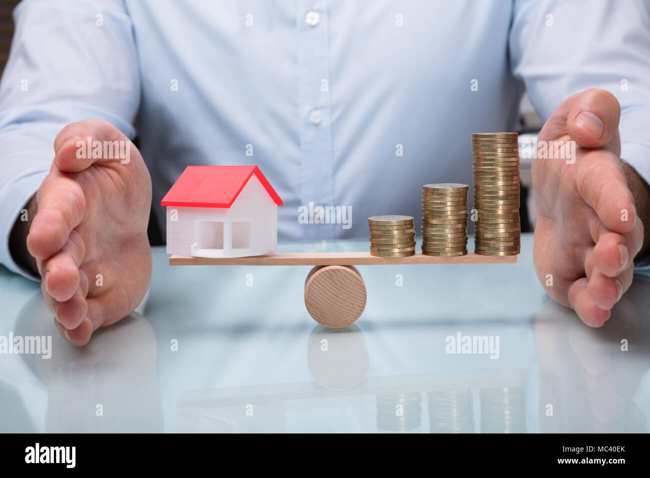 Der Unternehmer schützende Hand Balance zwischen Haus Modell und zunehmende Gestapelte Münzen auf Wippe Stockfoto