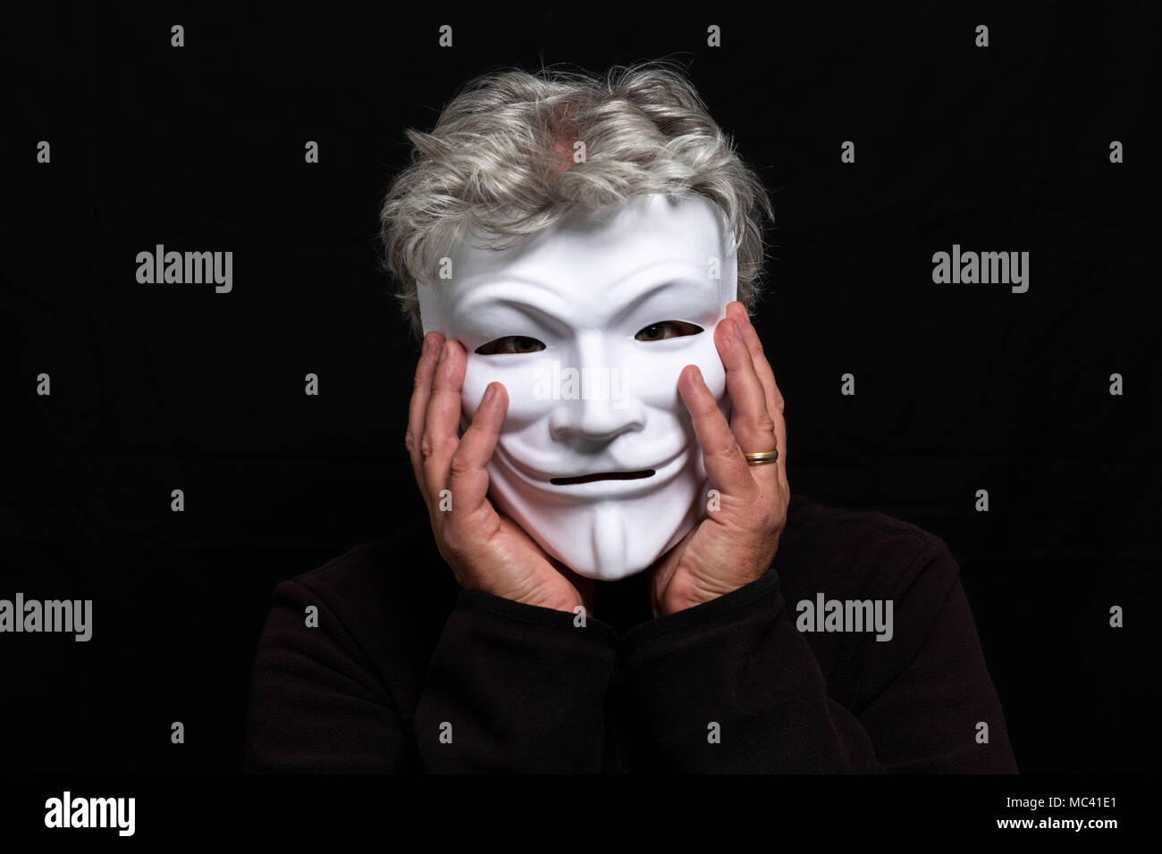 Grauhaariger Mann in anonymen Maske sein Gesicht in seinen Händen halten Stockfoto
