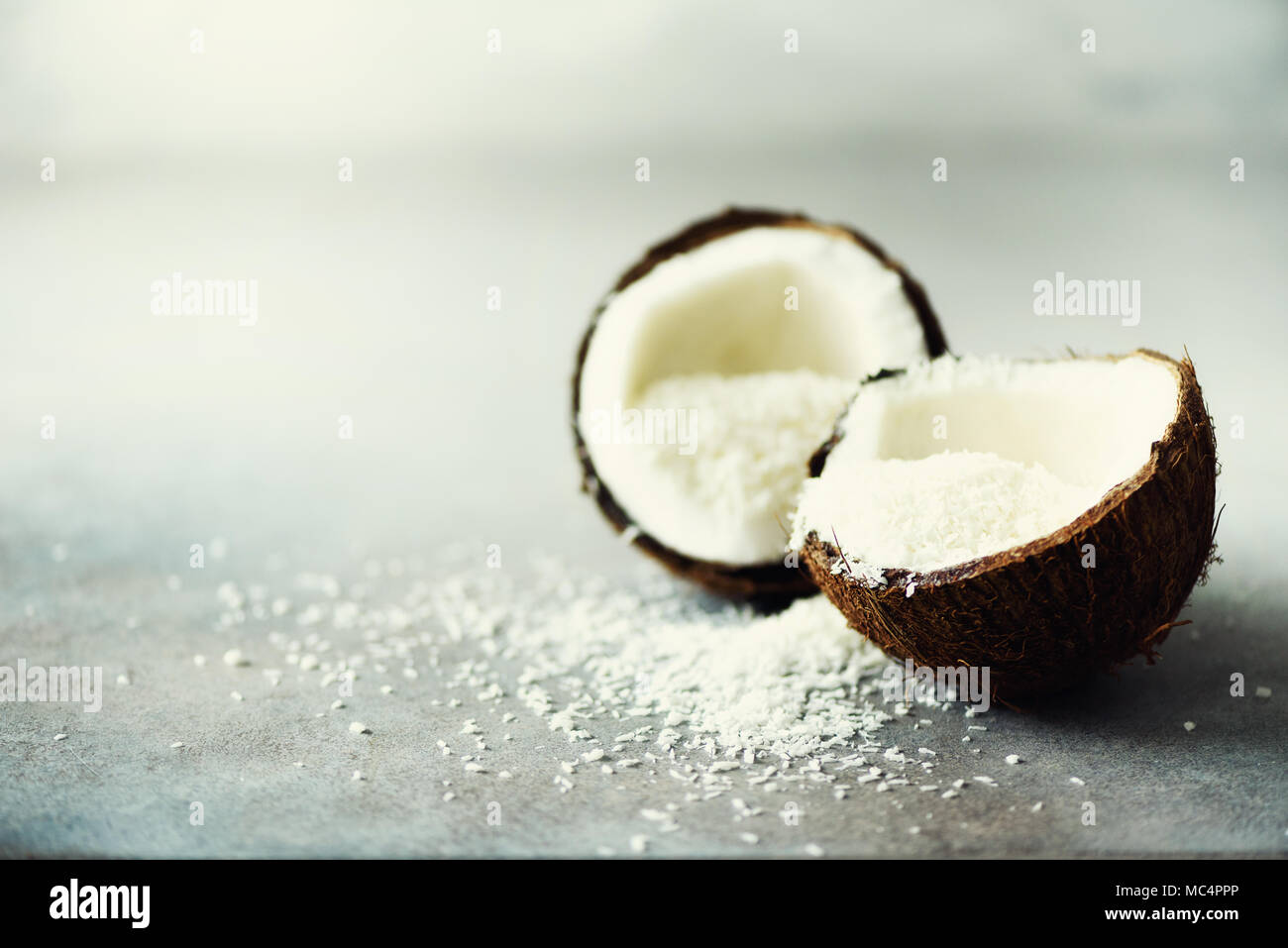 Coconut fuit Hälften mit Kokos Späne auf grauem Beton Hintergrund. Copyspace Stockfoto