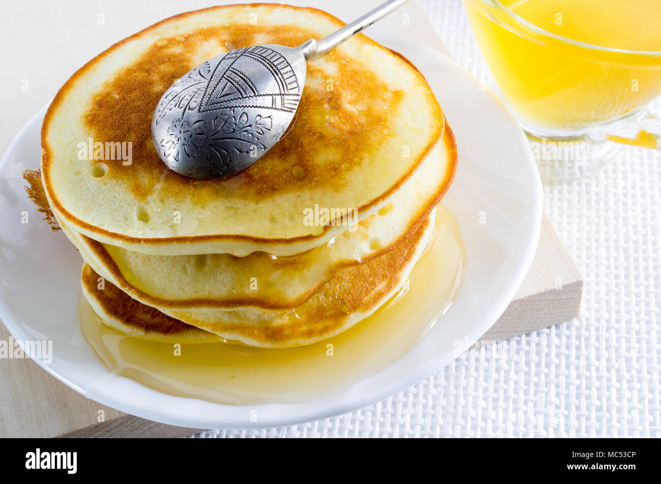 Pfannkuchen mit Honig und silbernen Löffel auf einer weißen Platte für ein süßes Frühstück Stockfoto