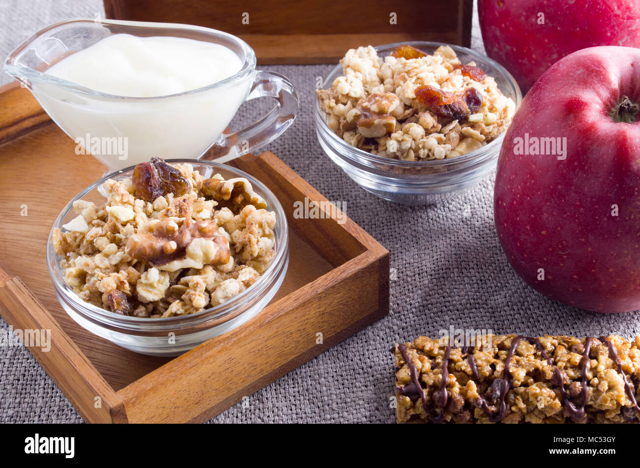 Nützliche Produkte für das Frühstück. Müsli mit Nüssen und Rosinen, Äpfel und Joghurt auf einem grauen Tischdecke closeup Stockfoto
