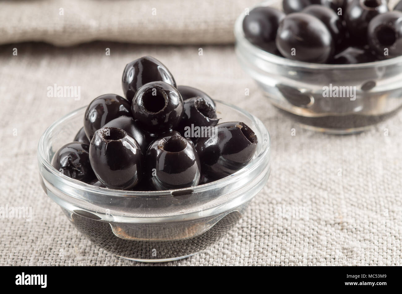 Schwarze Löcher marinierte Oliven im Glas Schale auf einem Hintergrund von grauen Sackleinen Stockfoto