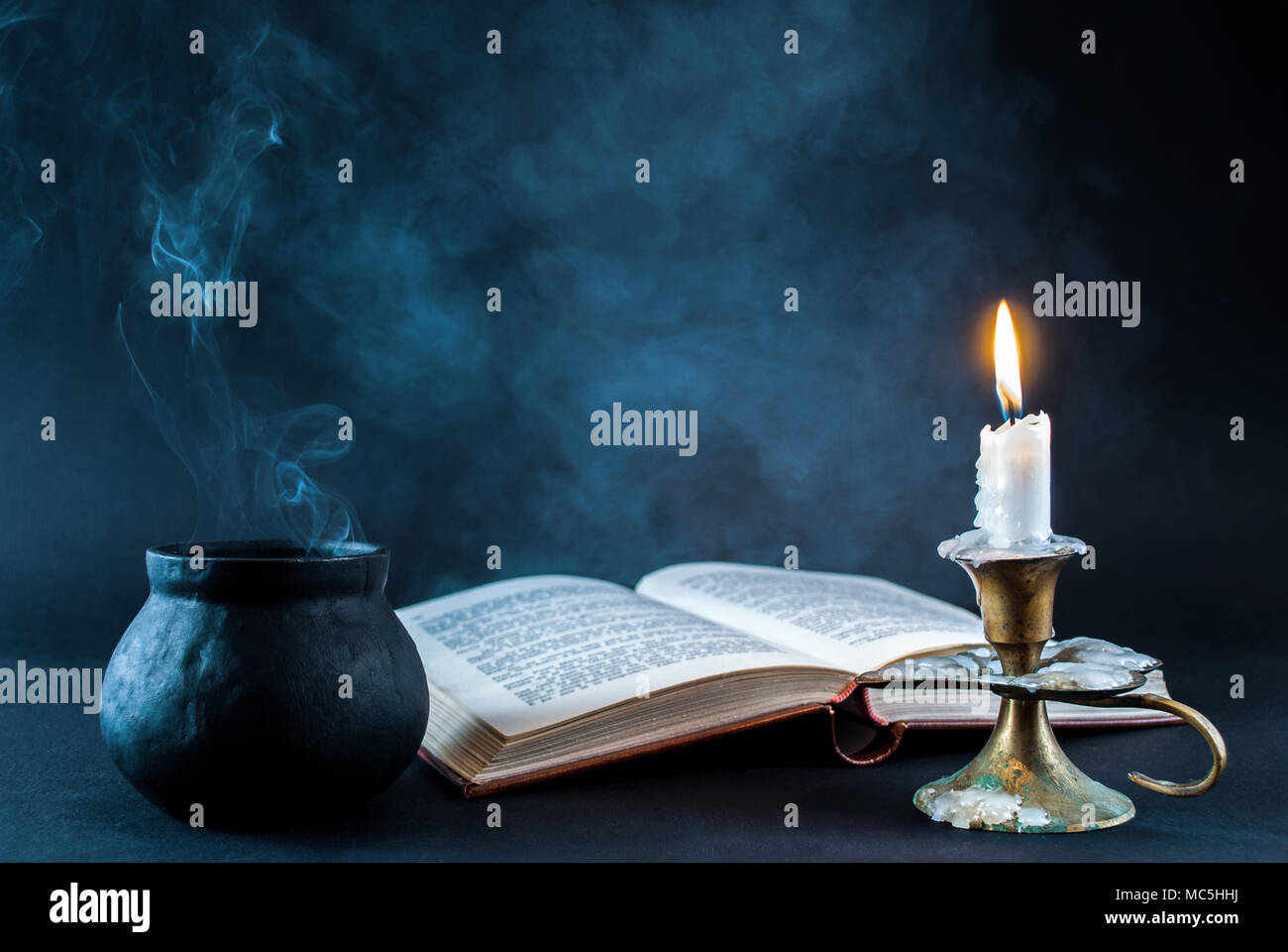 Kerze im Leuchter brennen und rauchigen Topf und alten Buch öffnen auf dunklen und weißen Hintergrund. Halloween Konzept Stockfoto