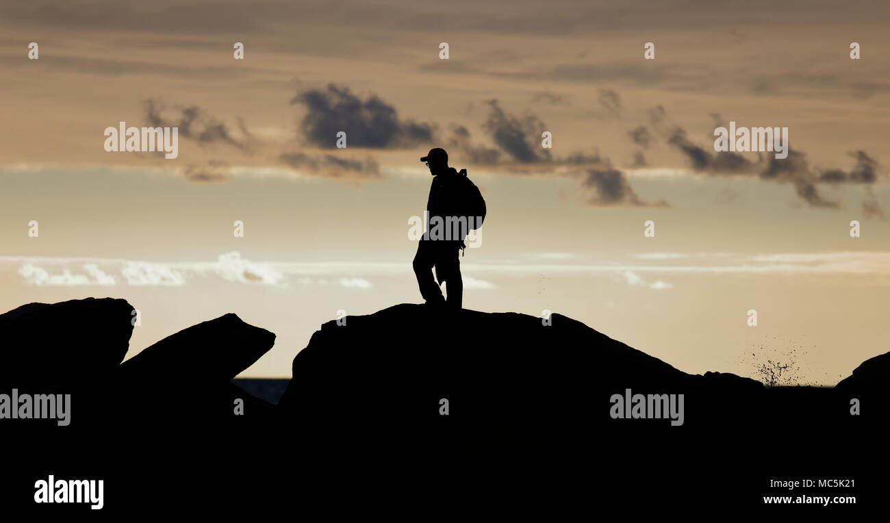 Panoramablick - style Silhouette eines Mannes (nicht identifizierbaren) standen auf den Felsen an der interessanten Abend Himmel suchen. Stockfoto