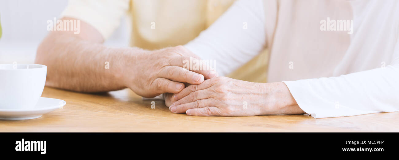 Eine Nahaufnahme der faltigen Armen auf einem Tisch, ein älterer Mann seine Hand auf den Händen eine ältere Frau Zuneigung zeigen und ihre Unterstützung der Holding Stockfoto
