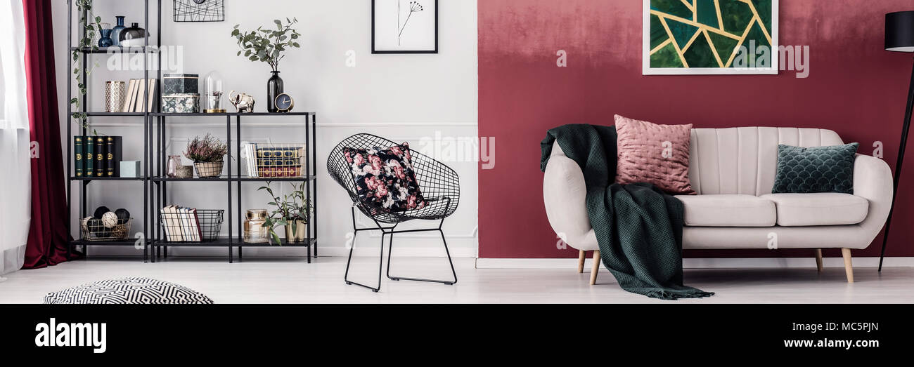 Reich, gemütliche Wohnzimmer Einrichtung mit weißen Wänden und Burgund, beige Sofa, Metall net Stuhl und ein Bücherregal mit Dekorationen Stockfoto