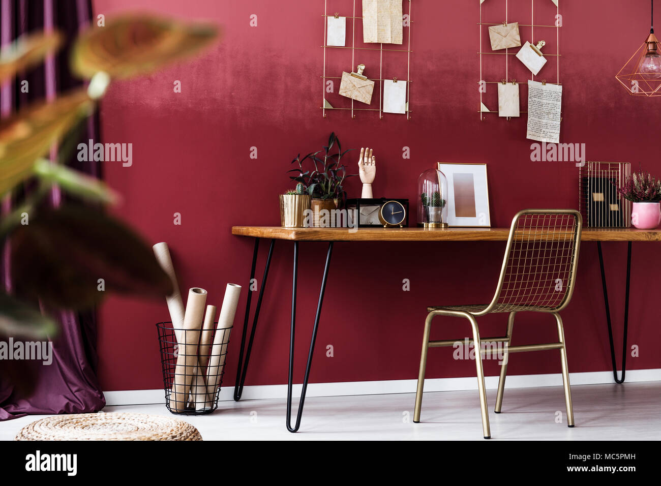 Gold Stuhl am Schreibtisch mit Uhr und Poster im gemütlichen roten Arbeitsbereich Interieur mit cherry Wand Stockfoto