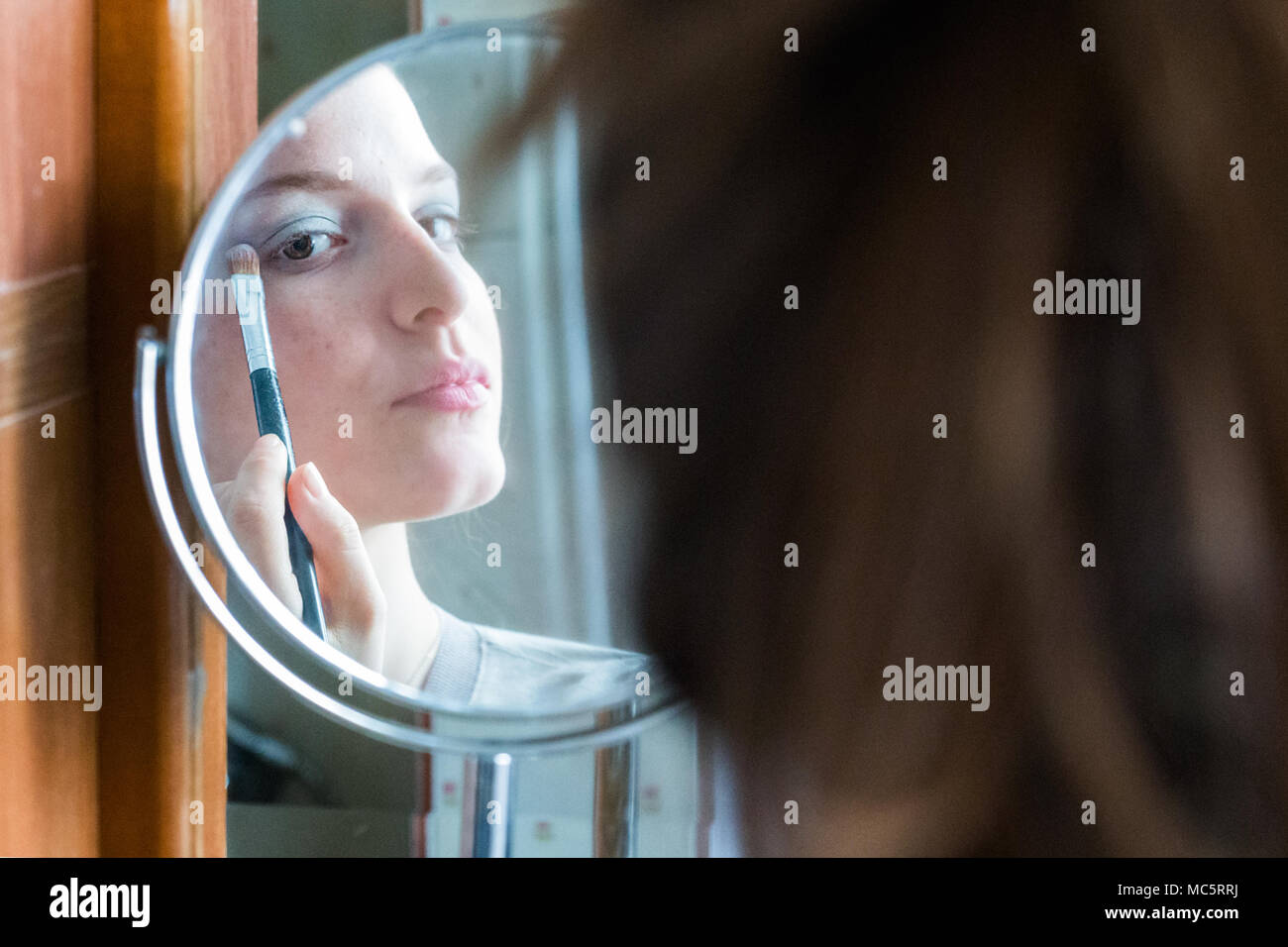 Jugendlicher Mädchen Anwendung Lidschatten ihr Spiegelbild auf einem runden Spiegel zu Hause suchen Stockfoto