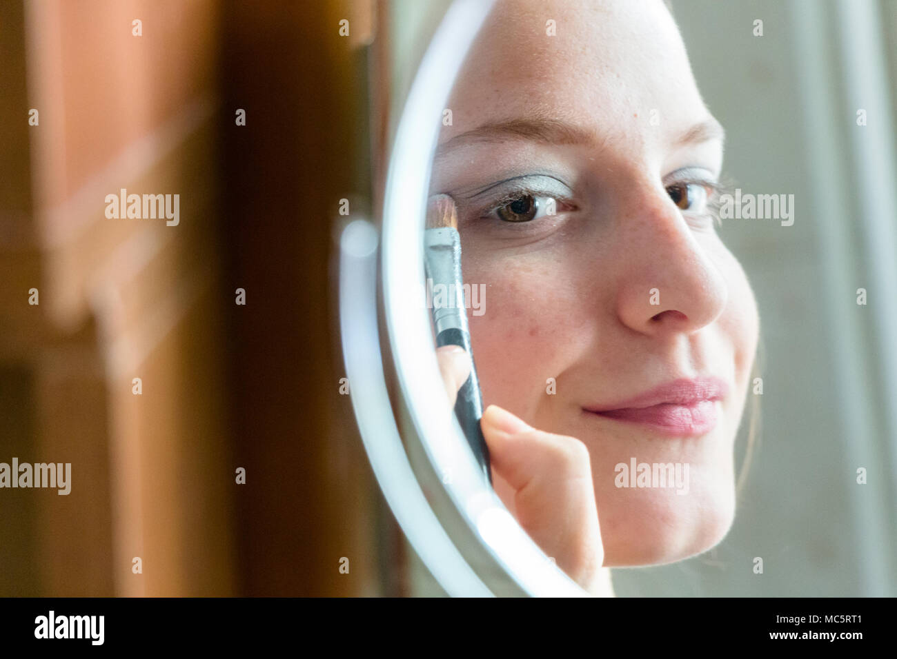Jugendlicher Mädchen Anwendung Lidschatten ihr Spiegelbild auf einem runden Spiegel zu Hause suchen Stockfoto
