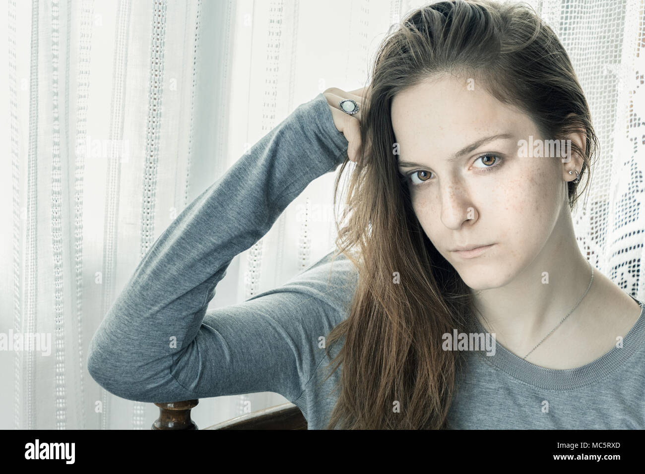 Jugendlicher Mädchen, zu Hause zu sitzen, mit der Hand auf dem Kopf suchen Kamera ernst, besorgt. Stockfoto