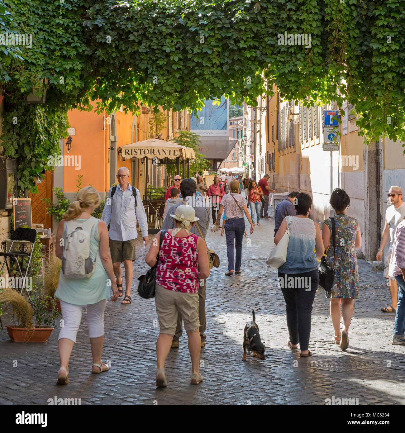 Menschen gehen auf einer gepflasterten Straße vorbei an Restaurants mit Sitzgelegenheiten im Freien in Rom, Italien, im Sommer. Stockfoto
