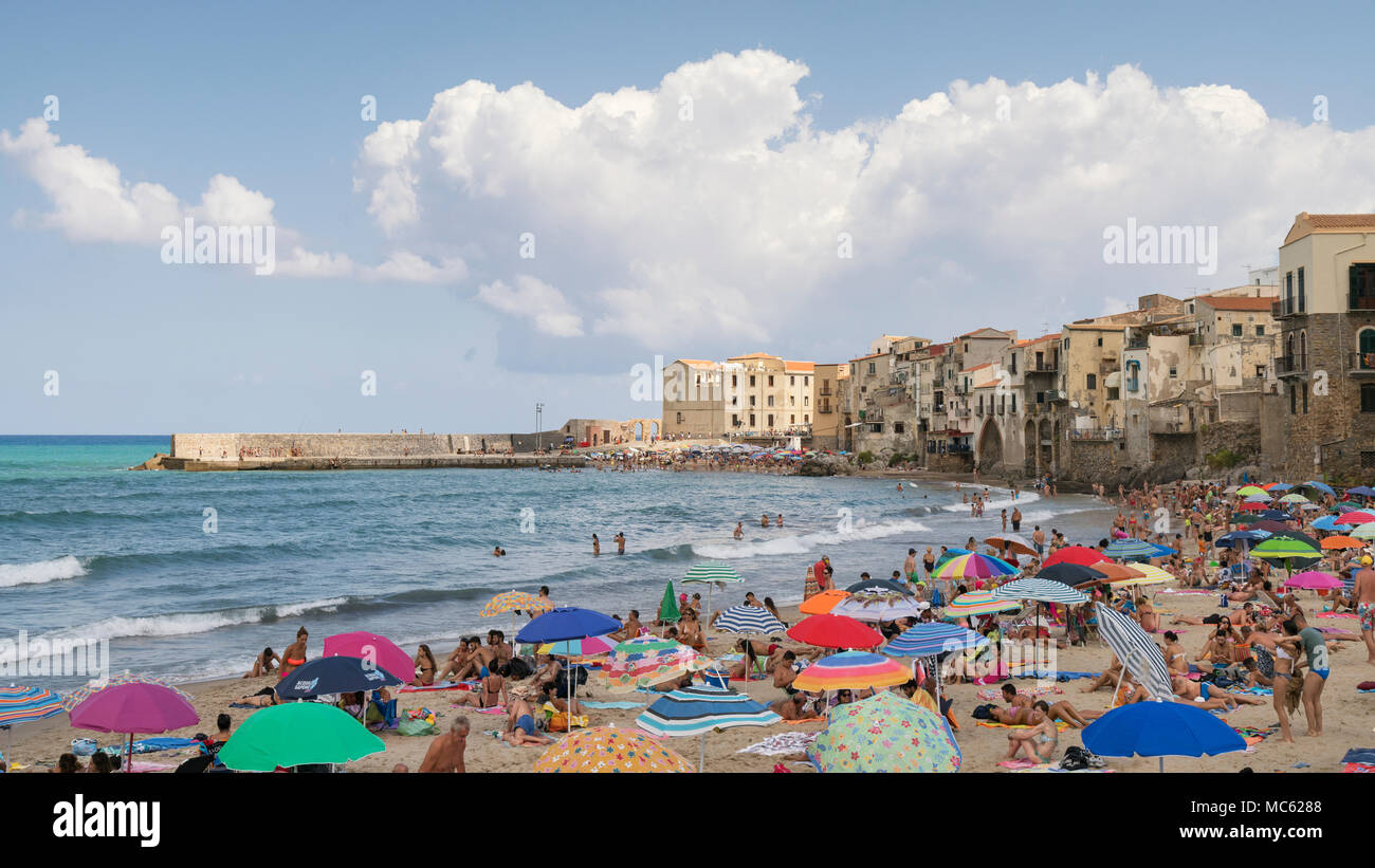 Cefalu, Sizilien, Italien, Menschenmassen Abdeckung der Sandstrand ihren Urlaub auf einem hellen, sonnigen Tag im August genießen Sie die Altstadt mit Gebäuden als Bac Stockfoto