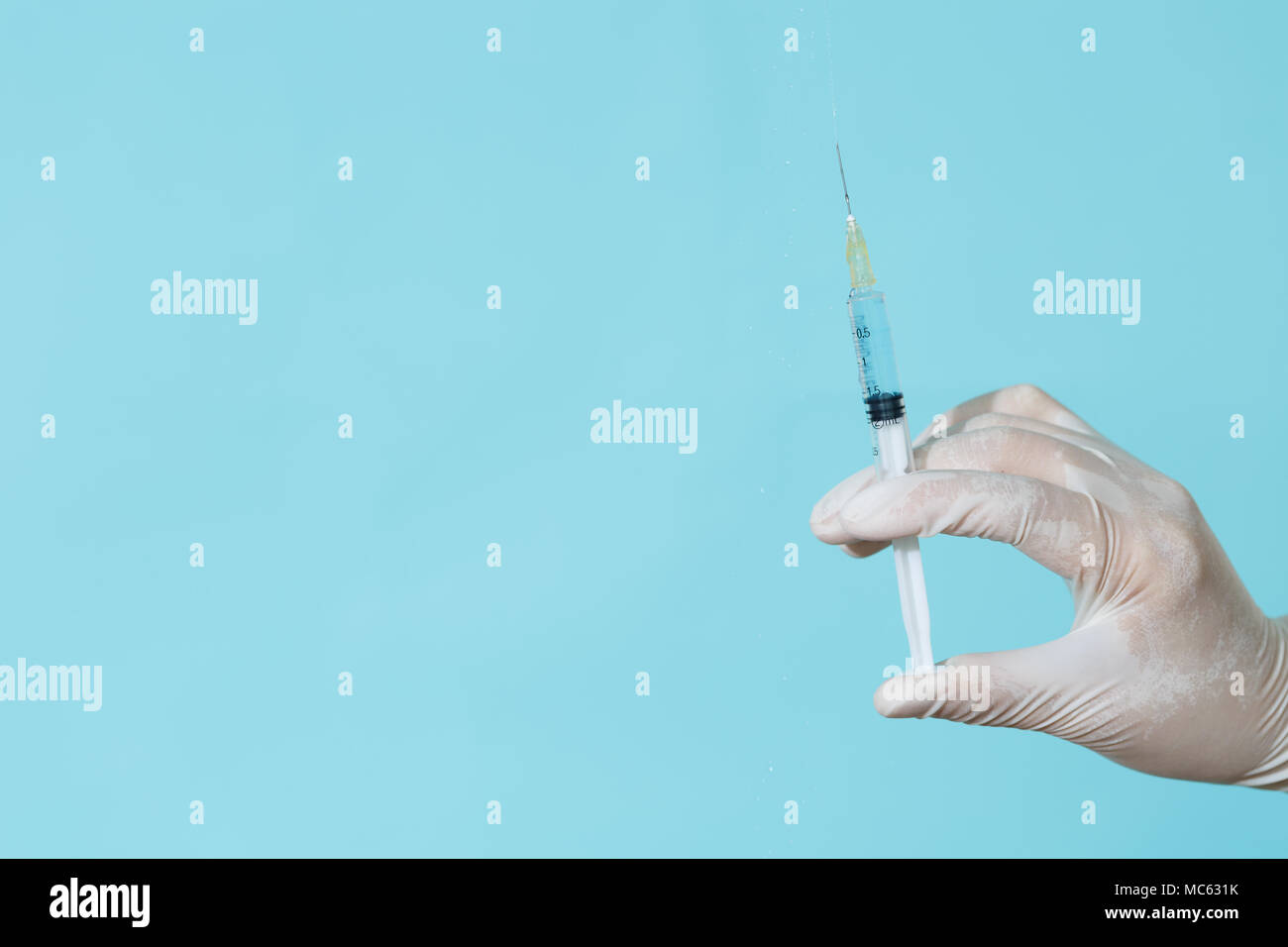 Eine behandschuhte Arzt hält eine Spritze auf einem blauen Hintergrund Stockfoto