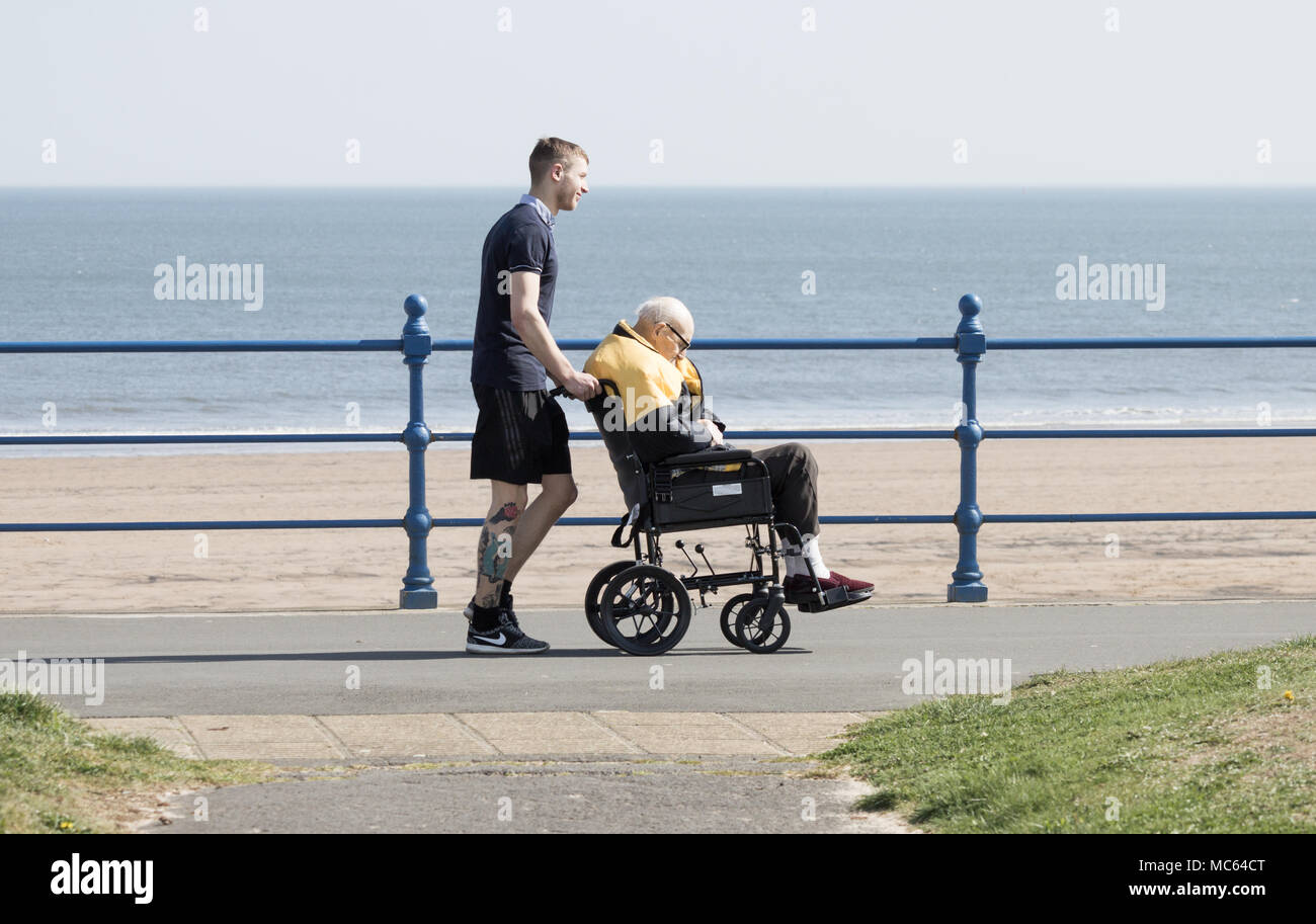 Junger Mann (eventuell Pflegeperson) drücken älterer Mann im Rollstuhl an der Küste. Großbritannien Stockfoto