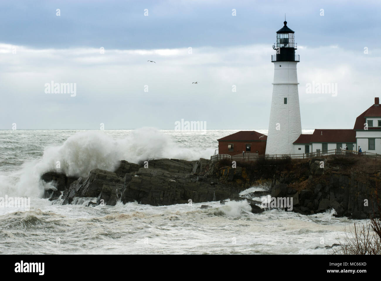 Sonne bricht durch die gewitterwolken als riesige Wellen durch Portland Head Lighthouse in Maine bei Flut. Stockfoto