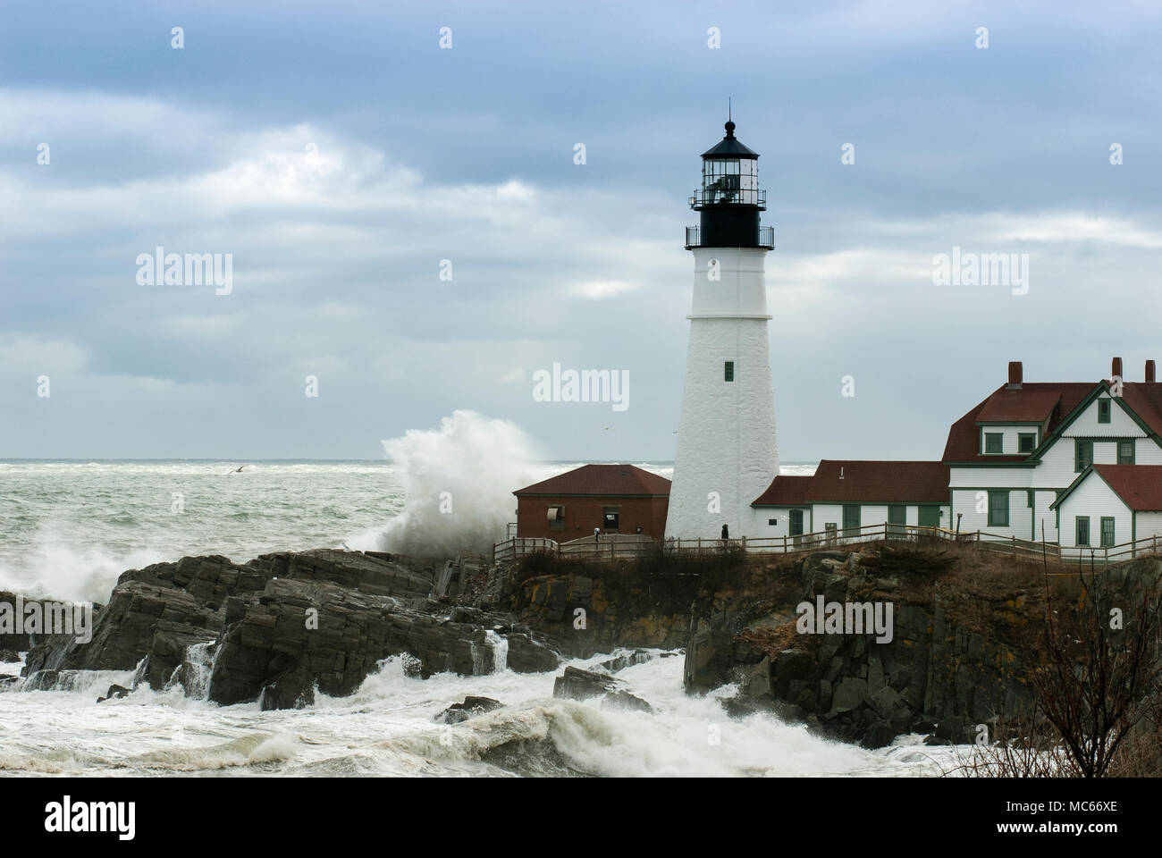 Riesige Wellen gegen Portland Head Lighthouse wie Sonnenlicht bricht durch Gewitterwolken. Es ist der älteste Leuchtturm in Maine und die zweitälteste Stockfoto
