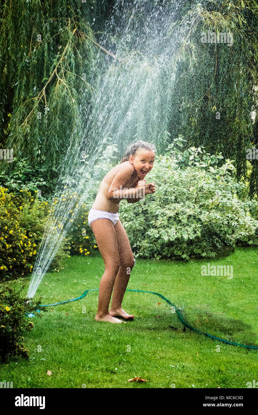 Junge Mädchen Spaß haben, während sie unter Garten Brunnen im heißen Sommer Tag stehen. Stockfoto