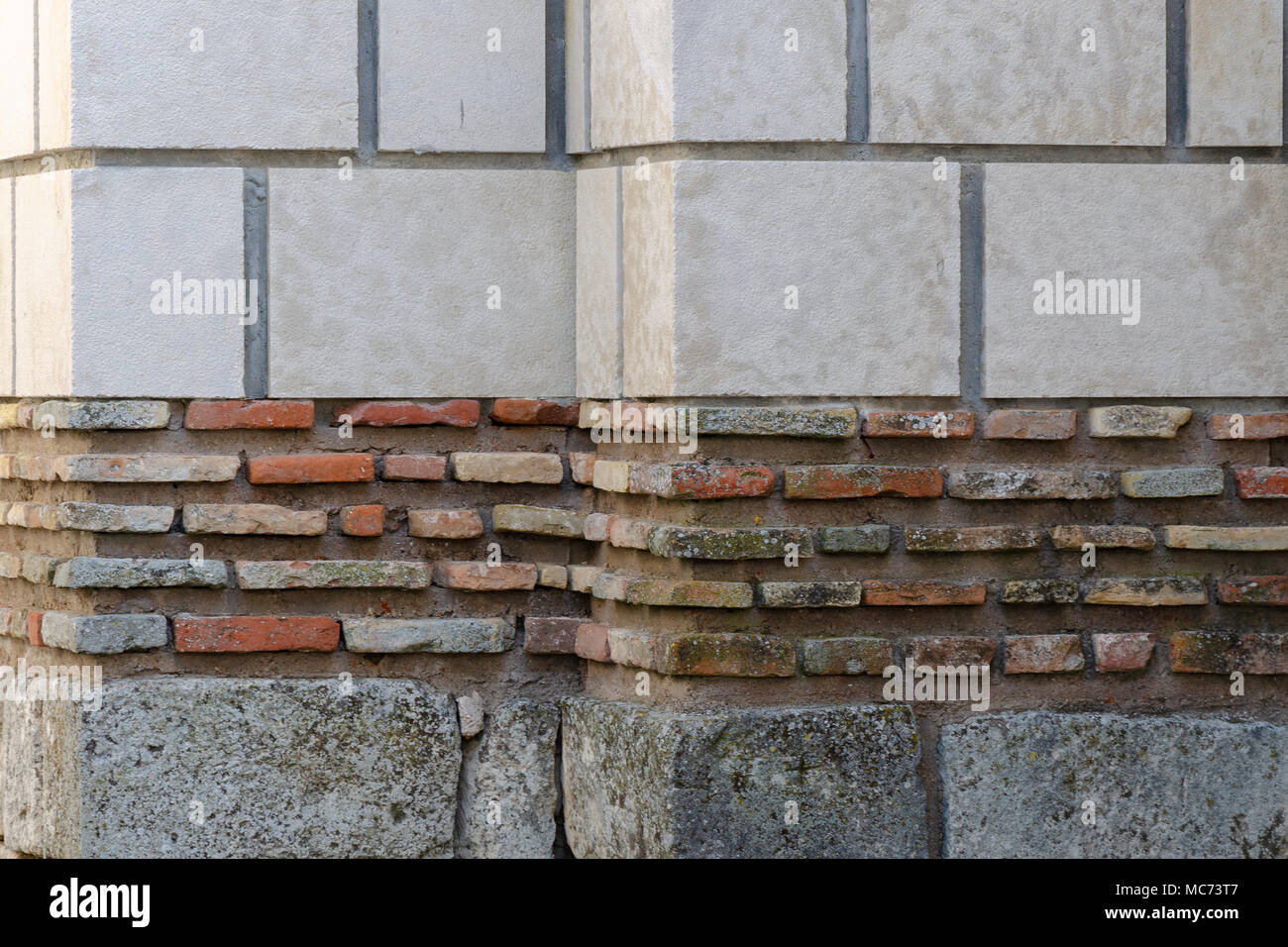 Verwitterte Wand aus Steinen mit verschiedenen Farbe und Größe, große weiße Blöcke oben, kleine rote Steine in der Mitte und die grauen Blöcke auf der Unterseite Stockfoto