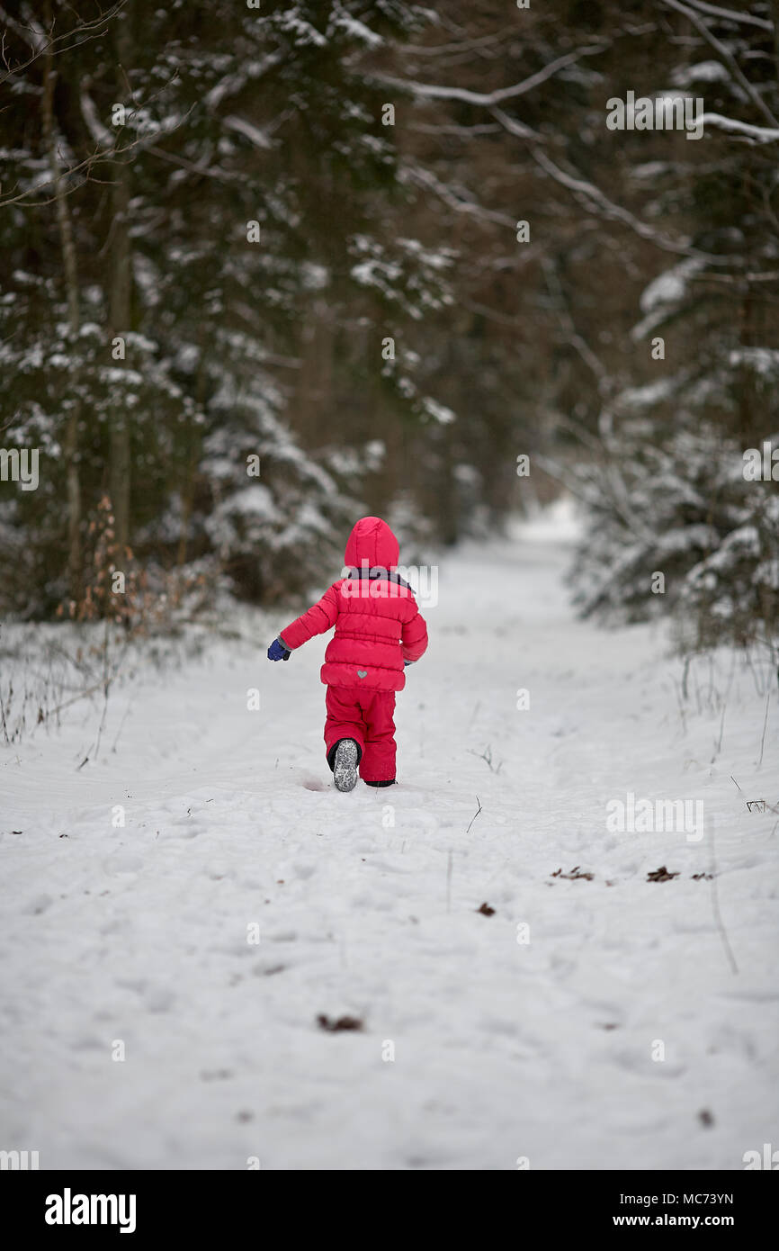 Süße kleine Baby Mädchen mit roter Jacke und Hose spielt in der Forest Park im Winter. Zurück anzeigen Stockfoto