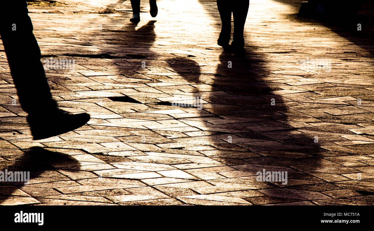 Blurry Beine Silhouetten und Schatten von Menschen zu Fuß auf Stadt gemusterten Platz im Sonnenuntergang Stockfoto