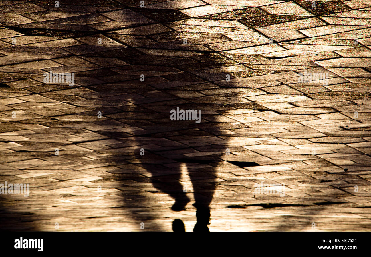 Verschwommene Schatten Silhouette einer Person, die auf Stadt gemusterten Bürgersteig in sepia Ton Stockfoto