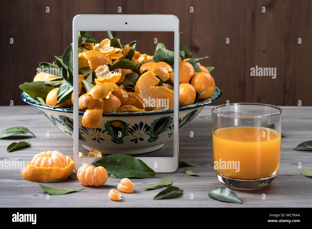 Weiß mobilen Tablet Stand vor der Keramik Teller gefüllt frische Mandarinen auf grau Holztisch. Pop up visuelle Wirkung. Kreative Zusammensetzung von Lebensmitteln. Stockfoto
