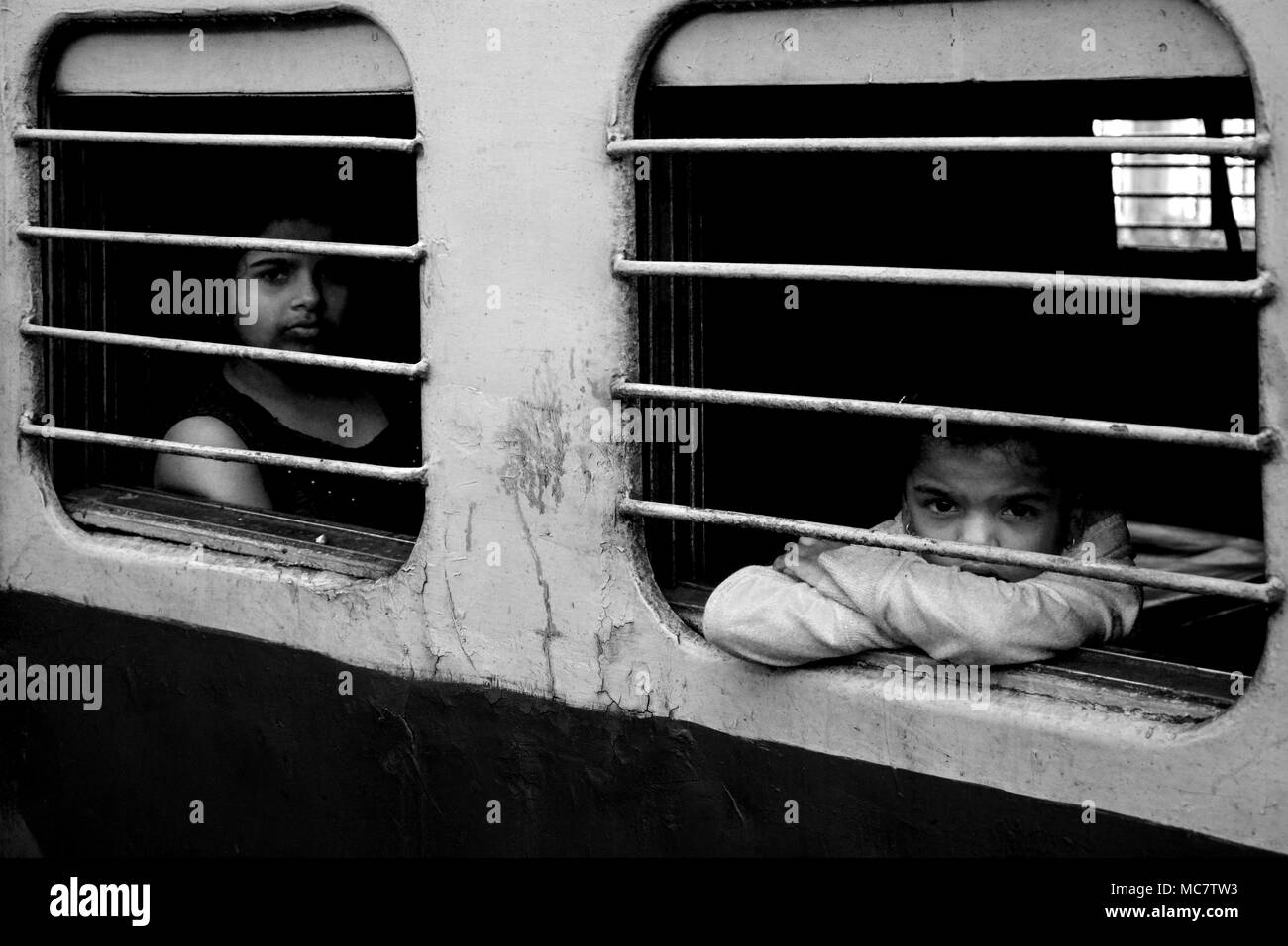 Mädchen und Jungen von den vergitterten Fenster eines indischen Zug, Mumbai gebunden. Schwarz und Weiß. Stockfoto
