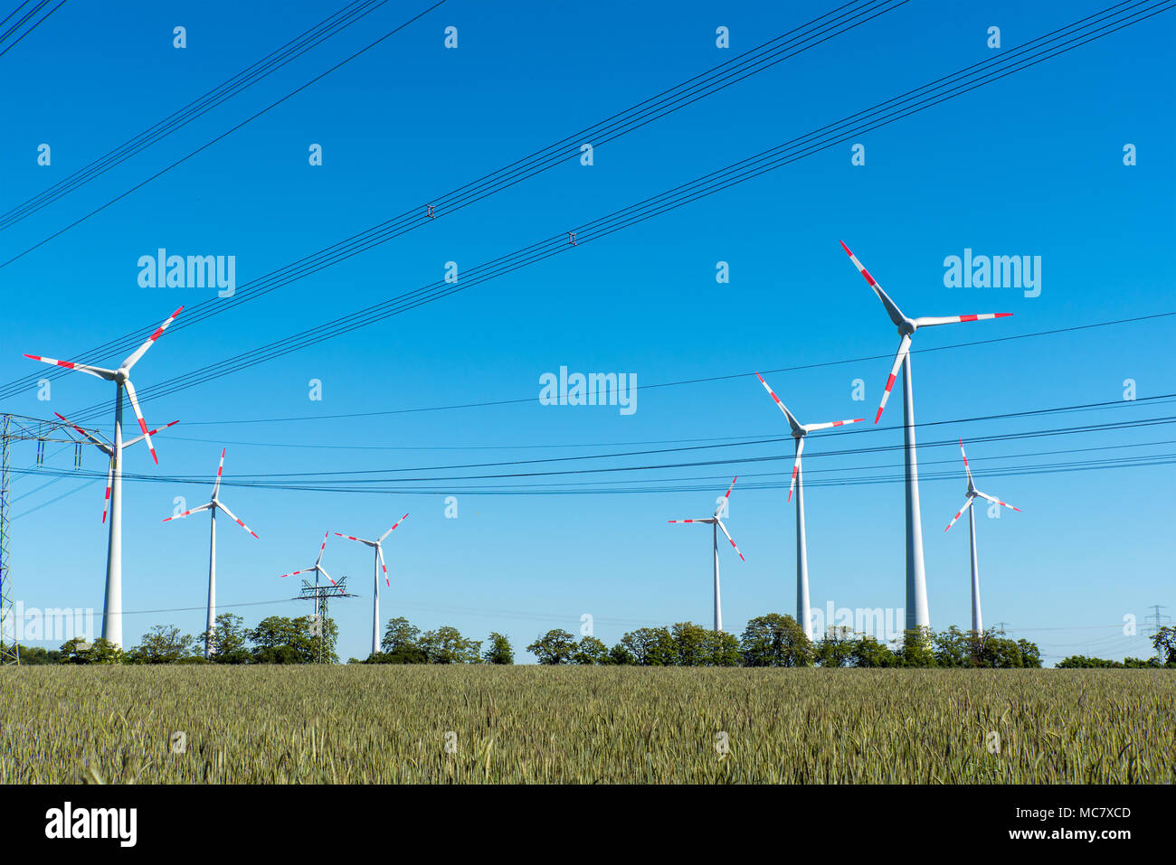Windenergieanlagen und Versorgungsleitungen an einem sonnigen Tag in Deutschland gesehen Stockfoto