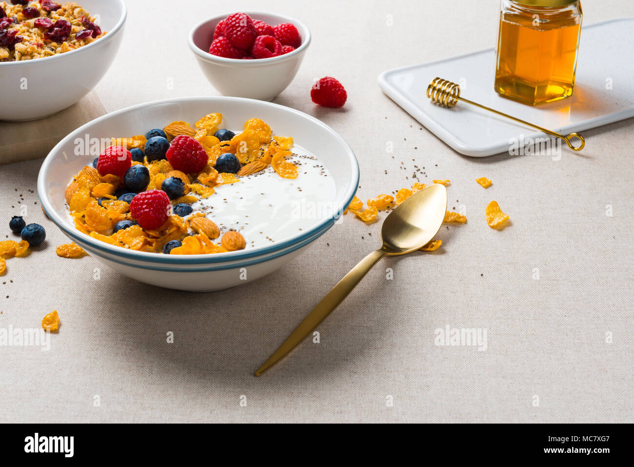 Gesundes Frühstück. Corn Flakes mit Joghurt, Mandeln, Blaubeeren, Himbeeren und Chia Samen. Mit Ahornsirup serviert, Müsli mit getrockneten Cranberries. Stockfoto