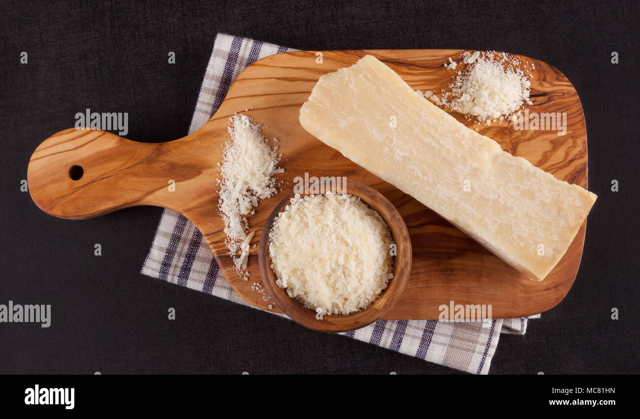 Gerieben und ganze Stück Parmesan auf Holzbrett auf der schwarzen Oberfläche von oben. Stockfoto
