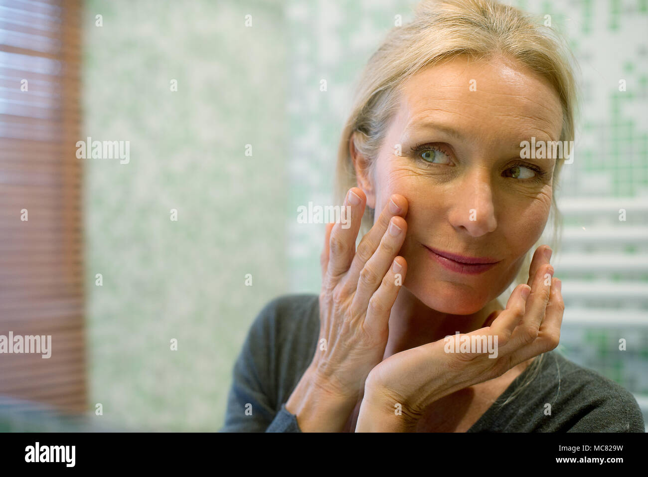 Reife Frau an der Reflexion im Spiegel zu betrachten, mit der Hand auf die Wange Stockfoto