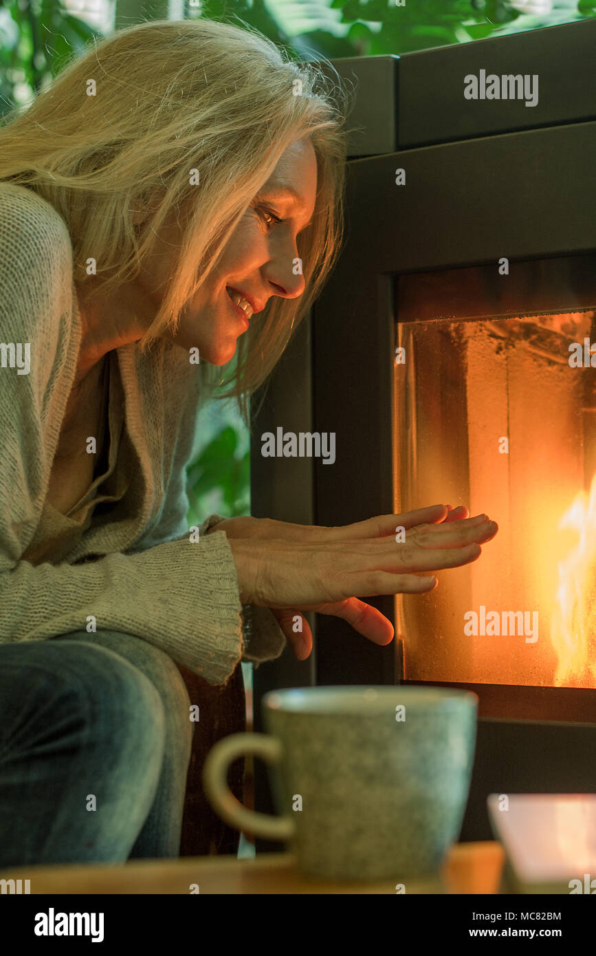 Reife Frau wärmen Ihre Hände durch Kamin Stockfoto