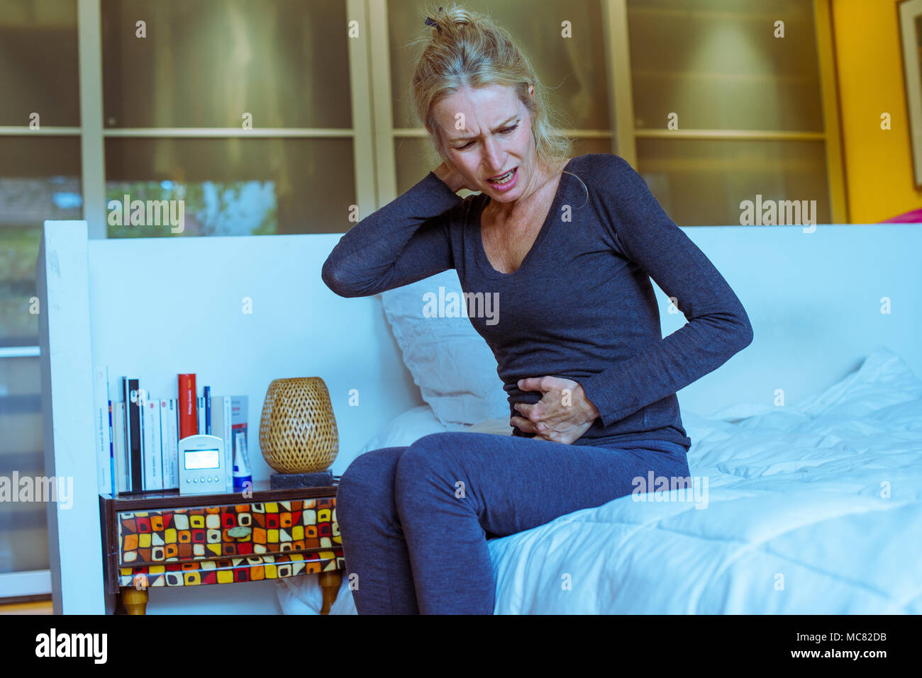 Reife Frau sitzt auf dem Bett mit Hand auf Magen und gequälten Gesichtsausdruck Stockfoto