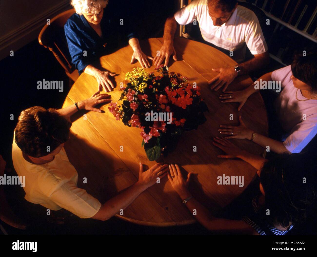 Eine Gruppe von Menschen an einem Tisch, mit den Händen berühren, mit dem Ziel, die Ladung der Atmosphäre in einer Weise förderlich für die geisterbeschwörung hellsichtig. Die Blumen werden gesagt, Kontakt mit den Geistwesen zu erhöhen. Stockfoto