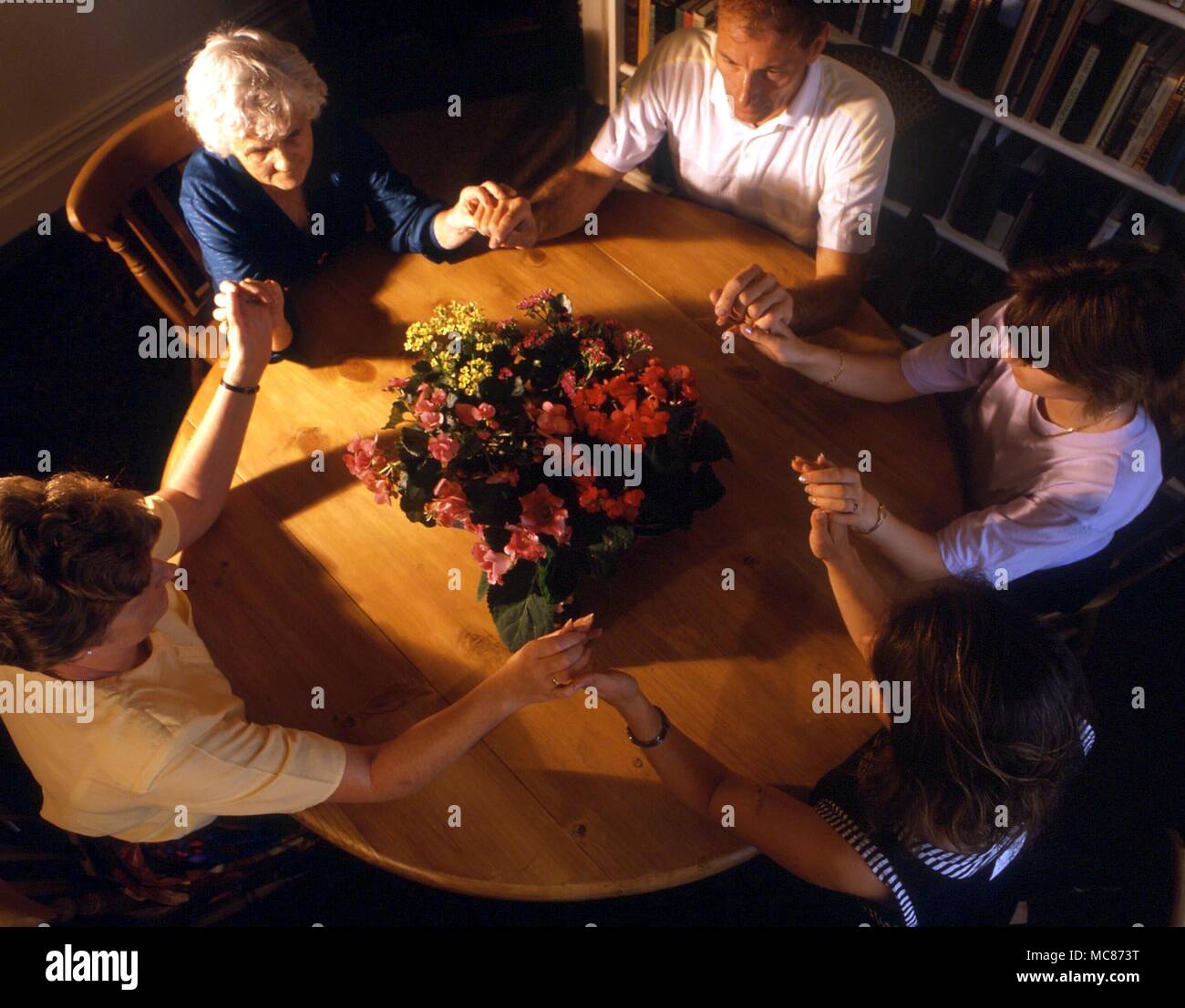 SEANCES. Eine Gruppe von Personen sitzen um einen Tisch mit den Händen berühren, mit dem Ziel, die Ladung der Atmosphäre in einer Weise förderlich für die geisterbeschwörung slarivoyantly. Die Blumen werden gesagt, Kontakt mit den Geistwesen zu erhöhen. Stockfoto