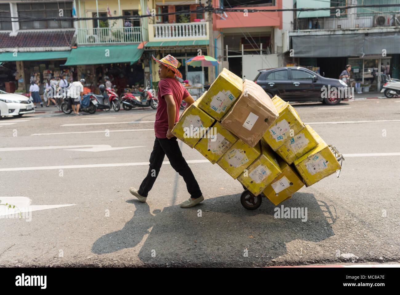 Ein Arbeiter in der Bangkok Blumenmarkt schiebt produzieren und Güter auf einer Sackkarre in Stockfoto