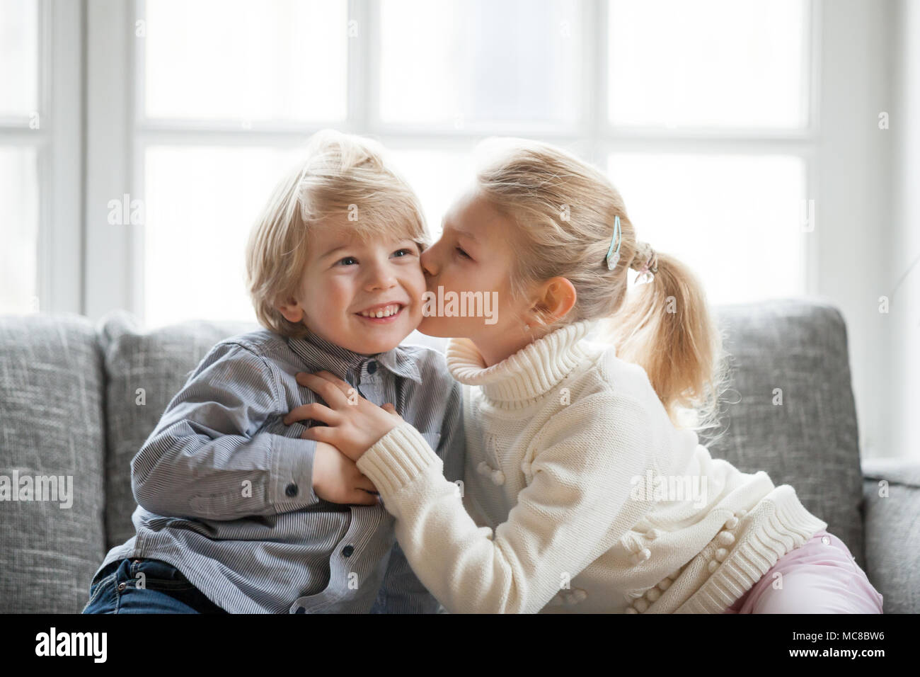 Ältere Schwester umarmen wenig jüngeren Bruder zu Hause, Kind Mädchen küssen Süß schüchtern lächelnd Vorschule junge auf Wange, glückliche Kinder sich gemeinsam amüsiert, l Stockfoto